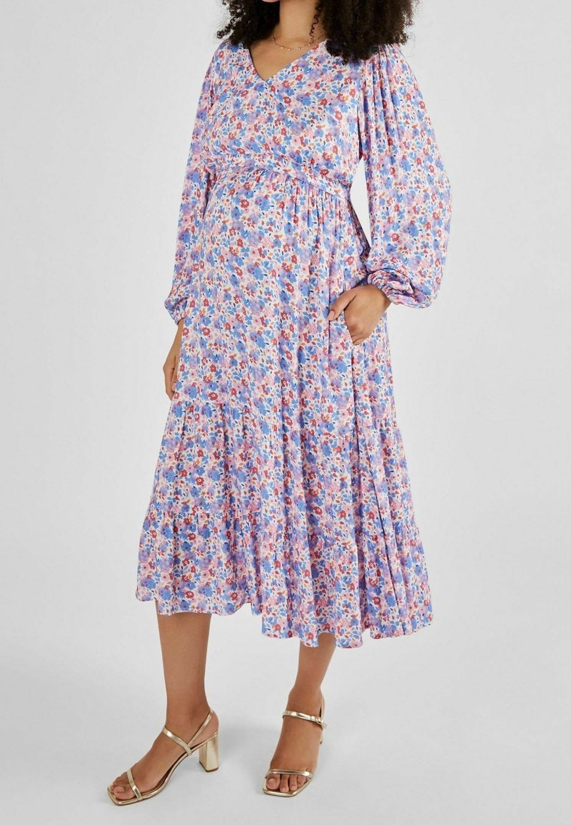 Vestido midi floral con mangas largas abullonadas en púrpura, rosa y azul, que presenta un diseño cruzado, cintura fruncida y bolsillos laterales. Sandalias de tacón bloque dorado.