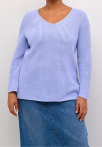 Pull en tricot violet clair avec un col en V et des manches longues, tissu texturé, associé à une jupe en denim avec une couture en biais.