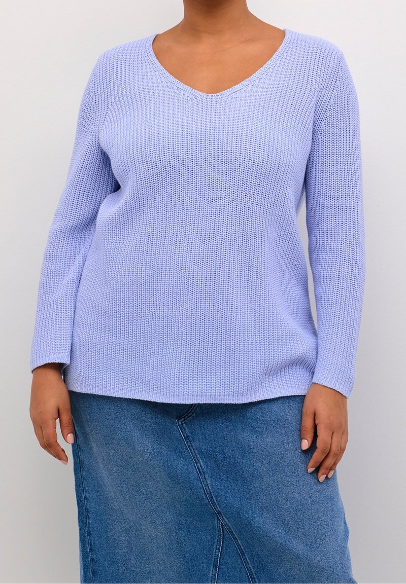 Pull en tricot violet clair avec un col en V et des manches longues, tissu texturé, associé à une jupe en denim avec une couture en biais.