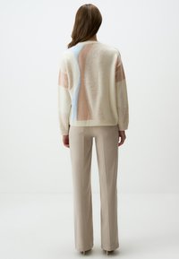 Maglione a girocollo color crema, con blocchi di colore pastello in rosa, blu e crema. Tessuto morbido, vestibilità rilassata. Abbinato a pantaloni beige.