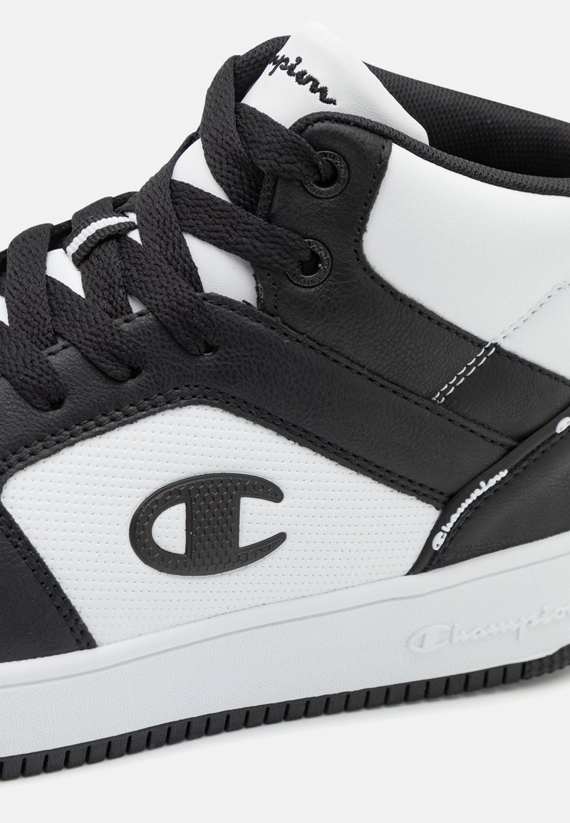 Schwarzer und weißer High-Top-Sneaker aus synthetischem Leder, ausgestattet mit einem strukturierten Einsatz, schwarzen Schnürsenkeln und einem auffälligen Markenlogo an der Seite.