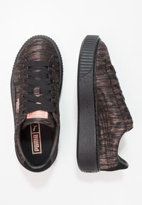 Baskets noires avec une tige texturée présentant un motif subtil, des lacets noirs et une semelle plateforme épaisse. Rehaussées d'une étiquette logo rose.