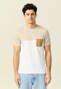 Lyhythihainen t-paita, jossa on kuviollinen kerma yläosa, valkoinen alaosa ja camel-värinen tasku. Valmistettu kevyestä kankaasta.