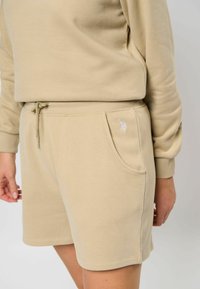 Beige katoenen shorts met een elastische tailleband, trekkoord en zijzakken. Voorzien van een klein geborduurd logo op de zak.