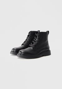 Botas de tobillo negras con cordones, con un diseño de patrón texturizado, punta redondeada, suela gruesa y una lengüeta en la parte trasera para facilitar el uso.