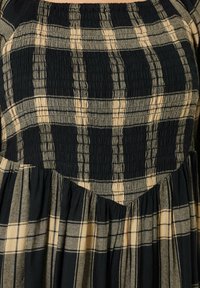 Vestido a cuadros negro y beige con corpiño fruncido, escote cuadrado y falda acampanada con textura recogida.