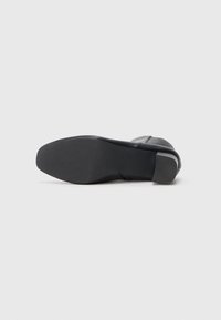 Czarny skórzany botek za kostkę z okrągłym noskiem, gładką fakturą i niskim, solidnym obcasem. Podeszwa jest płaska i lekko teksturowana.