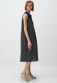 Abito senza maniche, lungo fino al ginocchio, di un blu scuro con strisce bianche verticali. Realizzato in tessuto leggero, presenta un colletto e una vestibilità morbida.