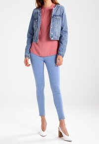 Spijkerjack, lichtblauw; roze blouse met gerafelde halslijn; lichtblauwe skinny jeans; witte hakken met blokhak; minimalistisch ontwerp.