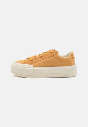 Niski sneaker z cholewką z płótna w kolorze żółtej musztardy, grubą białą gumową podeszwą i żółtymi sznurowadłami w kolorze dopasowanym, widoczny od zewnętrznej strony.