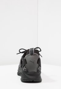 Chaussure de sport noire avec une tige texturée ornée d'accents gris, un col rembourré et une semelle extérieure en caoutchouc. Lacets fixés sur le dessus pour un ajustement optimal.