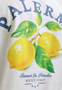 Deux citrons jaunes avec des feuilles vertes et un texte disant Palerme, Été au Paradis, Sicile Italie sur un tissu blanc.
