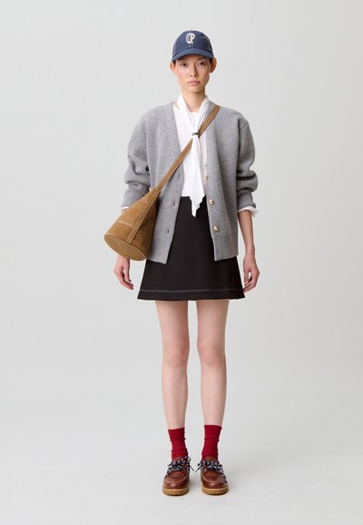 Cardigan grigio lavorato a maglia con bottoni dorati, camicetta bianca, gonna nera, borsa in camoscio marrone, calzini rossi e scarpe marroni con lacci decorati.