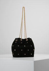 Borsa a secchiello in suede nero con borchie a diamante dorate, dotata di doppia tracolla a catena e chiusura a coulisse. Texture morbida, forma arrotondata.