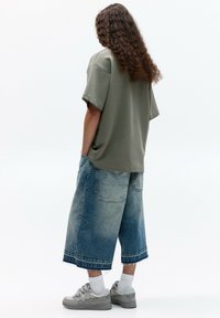 Overdimensioneret olivengrøn t-shirt, løs pasform, parret med knælange falmede blå denimshorts og grå sneakers, med hvide ankelstrømper.