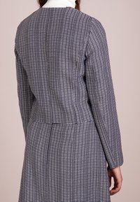 Cappotto a fantasia in un design a quadri blu navy e bianco, vestibilità sartoriale, con colletto alto e maniche lunghe. Tessuto con texture visibile.