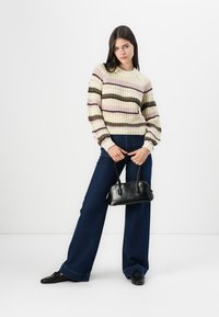 Maglione lavorato a maglia con strisce crema, rosa e marroni, abbinato a jeans a gamba larga blu scuro e una borsa nera. Tessuto liscio e vestibilità casual.