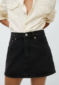Schwarzer Denim-Minirock mit hoher Taille, der Kupferakzentknöpfe und vordere Taschen aufweist. Textil mit strukturierter, klarer Design.
