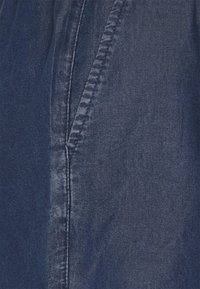 Tummansininen farkkukangas, jossa on pystysuoria ompeleita ja sileä koostumus. Kuva esittää materiaalin lähikuvan.