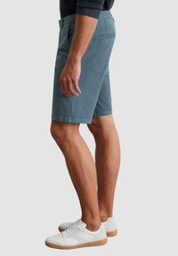 Shorts bleu clair en coton avec poches latérales. Le modèle porte des baskets blanches avec des semelles en caoutchouc. Design simple et coupe droite.