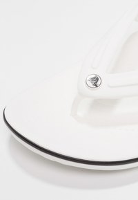 Valge suss, millel on tekstureeritud tallaosa, õhuke rihm ja must aktsent talla ääres. Rihmal on logo detail.