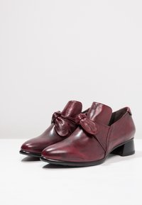 Chaussures en cuir bordeaux avec un bout pointu et un nœud décoratif sur la sangle, dotées d'un petit talon carré et d'une texture lisse.