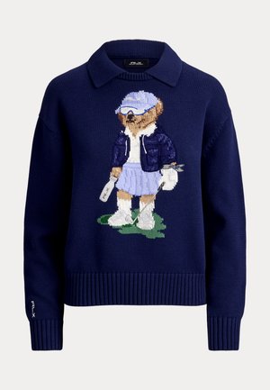 Maglione blu navy con colletto con un orsetto lavorato a maglia vestito con abbigliamento da golf, che tiene una mazza da golf e una bottiglia, in piedi sull'erba.