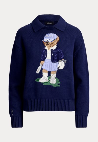 Pull bleu marine avec col présentant un ours en tricot vêtu d'une tenue de golf, tenant un club de golf et une bouteille, debout sur l'herbe.