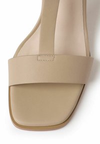 Beige open-toe sandalen met een brede band. Gemaakt van soepel synthetisch materiaal. Kenmerkt zich door een platte zool met ronde randen en minimale stiksels.