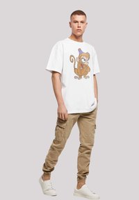 Hvit bomull t-skjorte med et tegneserieape-design, kombinert med beige cargo-bukser og hvite sneakers. Enkel og avslappet antrekk.