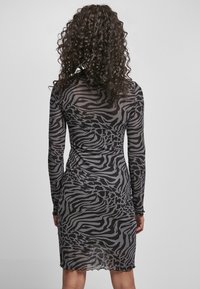 Sukienka z siateczki w czarno-szary wzór zebra, z długimi rękawami, dopasowany kształt, falbaniasty dół, półprzezroczysty materiał, podkreślony detal na plecach.