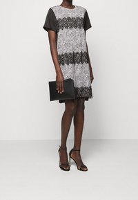 Kraťasové šaty s černým topem a vzorovaným šedým tělem, zdobené krajkovými detaily. Doplněné černými sandály na tenkých podpatcích a černou kabelkou.