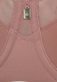 Rosa BH aus weichem Stoff mit Netzakzenten und einem kleinen metallischen Logotag in der Mitte. Glatte Textur mit genähten Details.