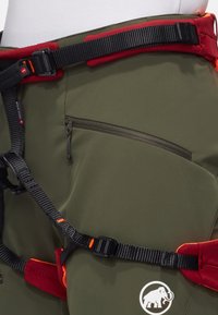 Grön klättersele med justerbara röda detaljer, ett svart midjebälte, en ficka med dragkedja och en logotyp av en elefant på den nedre sidan.