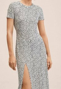 Robe à manches courtes en tissu blanc avec un motif tacheté noir, dotée d'une fente latérale pour plus de détails et d'une silhouette ajustée.