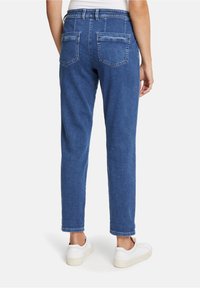 Pantalones de denim azul con un corte relajado, que cuentan con una cintura de altura media, bolsillos traseros y un dobladillo a la altura del tobillo. Combinados con zapatillas blancas.