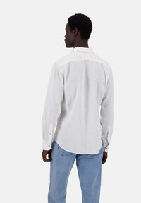 Weißes Langarmhemd mit Button-Down-Kravatte, leichtem Stoff und abgerundetem Saum; kombiniert mit hellblauen Jeans.