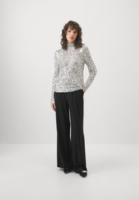 Sølv long-sleeve topp med paljetter og høy hals, parret med svarte vide bukser. Svarte sko med dekorative detaljer. Glatte teksturer.