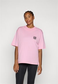 Tricou din bumbac roz, cu mâneci scurte, guler rotund și un buzunar cu model negru pe partea stângă. Proiectat pentru o croială lejeră.