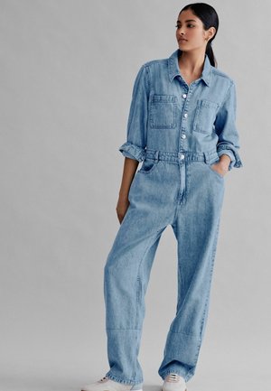 Salopette in denim di colore blu chiaro, dotata di chiusura a bottoni sul davanti, due tasche sul petto e una vestibilità comoda con maniche arrotolate e gambaletti affusolati.