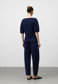 Mörkblå topp med vida ärmar och fyrkantig halsringning, tillsammans med matchande avslappnade byxor, båda i ett mjukt och följsamt material. Svarta slip-on skor.