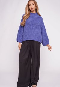 Purple, textured knit sweater with a high neck and wide sleeves, paired with black, flowy, wide-leg trousers, against a plain background.