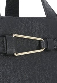 Dettaglio di una borsa a tracolla in pelle nera con un accento in hardware dorato e superficie testurizzata, che mette in evidenza un attacco a clip e cuciture.