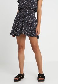 Jupe skater florale en bleu marine avec de petites fleurs roses. Tissu léger, taille cintrée, ourlet évasé, associée à des sandales tissées noires.