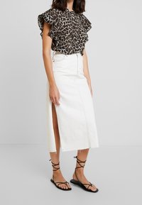 Blouse à imprimé léopard noir et beige avec manches à volants, associée à une jupe en denim blanc avec une fente à l'avant et des sandales noires à brides.