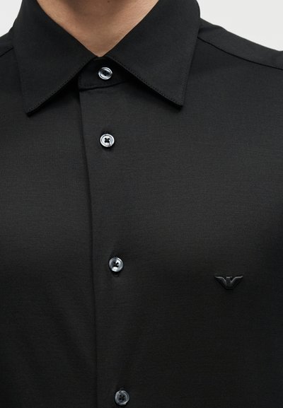 Μαύρο πουκάμισο με γιακά και κουμπιά μπροστά, με μικρό κεντημένο λογότυπο στο αριστερό στήθος.