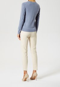 Pull en cachemire bleu à manches longues, col rond et ourlet côtelé, associé à un pantalon beige ajusté et des chaussures à talons hauts couleur crème.