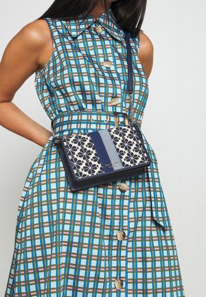 Hihaton ruudullinen mekko, jossa edessä napit ja vyö, yhdistetty tummansiniseen ja kermaan sävyiseen, sinisillä pystysuunnassa kulkevilla raidoilla koristeltuun kukkakuvioiseen olkalaukkuun.