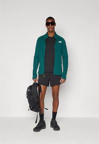 Modra jakna z zadrgo, črna majica s kratkimi rokavi in hlače; črn nahrbtnik; črni škornji; sončna očala; atletski dizajn; zračen material.