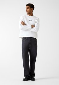 Biała bluza z długim rękawem z haftowanym napisem, w połączeniu z wysokim stanem ciemnoszarymi dżinsami i czarnymi butami. Prosty, luźny krój i konstrukcja.